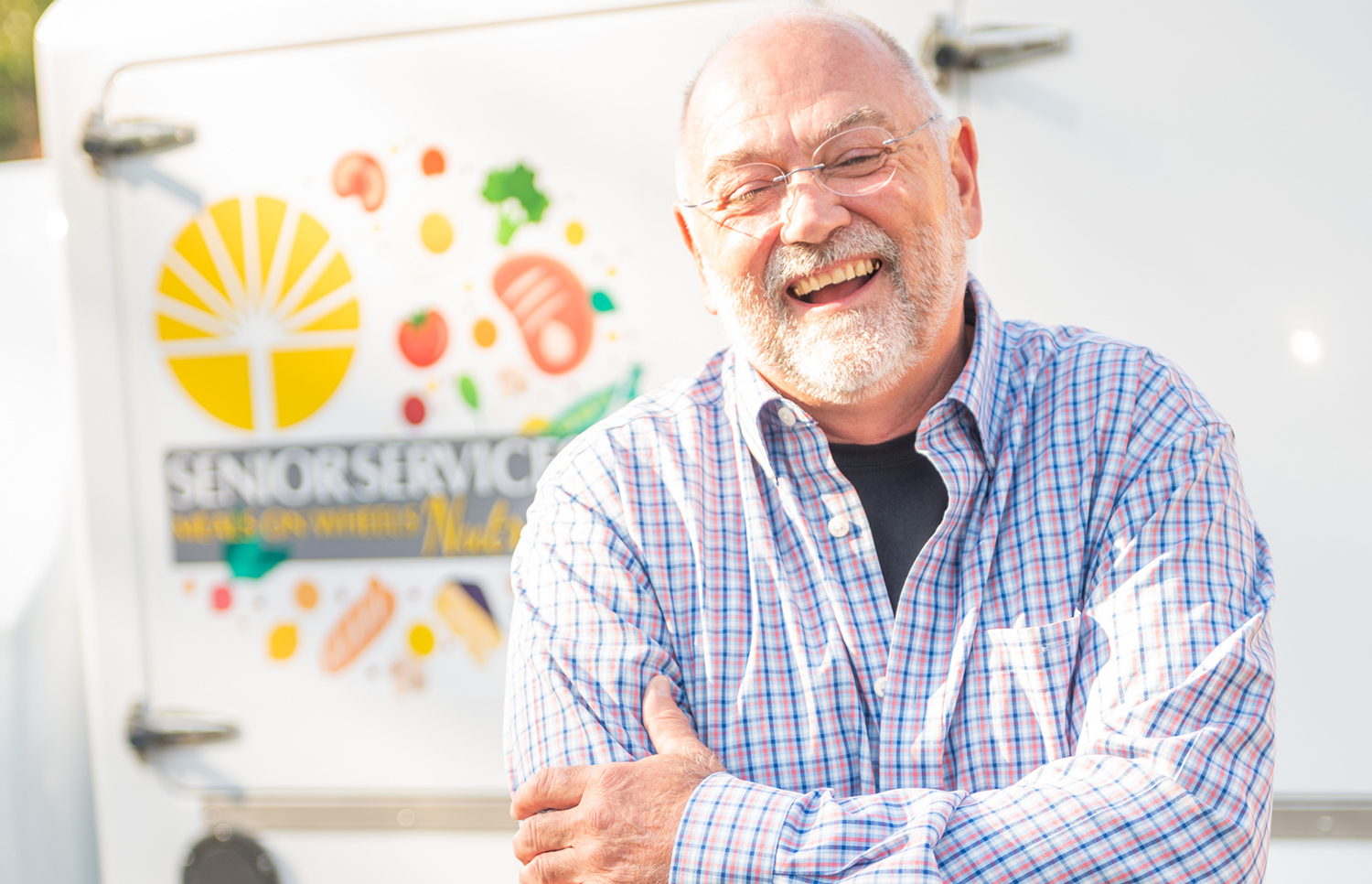 Meals on Wheels volunteer smiles while posing in from of a nutrition delivery van.